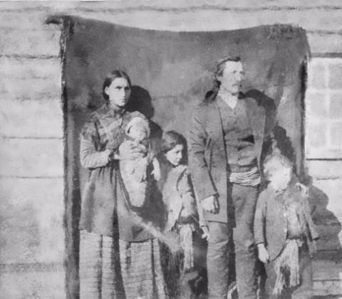 A black and white photo of a family, including a mother, father, and three kids. The photo appears to be very old.