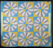A photo of Lossie Lane's Wagon Wheel Quilt. The quilt has a pattern of white and grey wheels on top of yellow and blue squares.