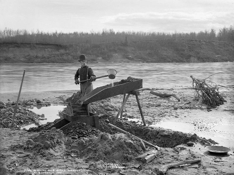 Historic black and white image of a gold panner using a sluice.