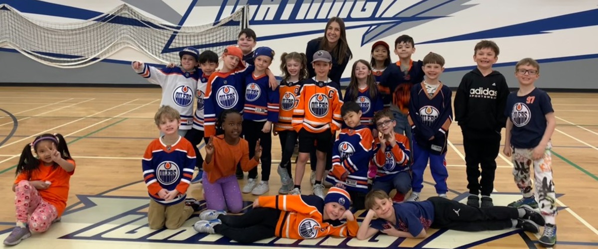A group of smiling students wearing Edmonton Oilers jerseys stand in a gym posing for a photo