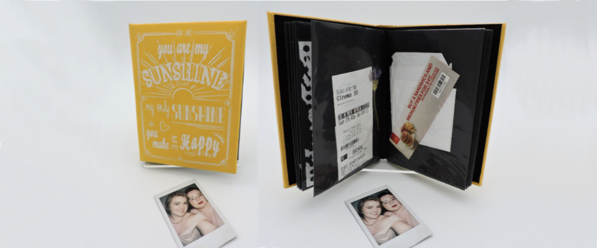 Two polaroid photos of Harper-Hugo and Will from their wedding. Above the photo on the left we see the cover of the scrapbook from the beginning of their relationship. The cover is yellow with the lyrics to "You are my Sunshine" in white.  On the right is the inside of the scrap book. It's opened to a page with a movie ticket and coupon.