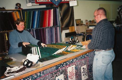 A woman and man choose from a number of green fabrics laid across a table