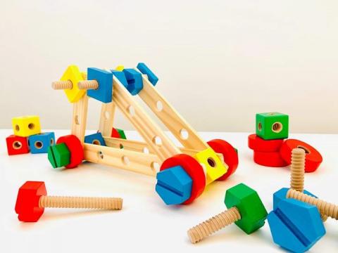 Brightly coloured toy nuts and bolts hold together wooden boards with holes. 