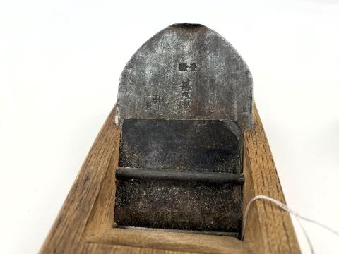 A close up of a metal blade on a wooden plane tool. Japanese characters are embedded in the metal blade. 