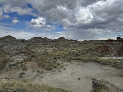 A landscape photo of dry looking hilly formations and a blue sky filled with clouds