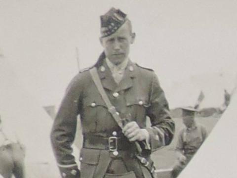 A faded vintage photograph of Solider William Frame looking stoically out at the camera. He is wearing his military uniform. You can see tents in the background.