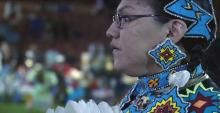 An Indigenous woman with beaded ceremonial clothes and jewelry gazes intensely to the right.