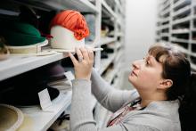 Julia Petrov looks up at a shelf full of historical hats.
