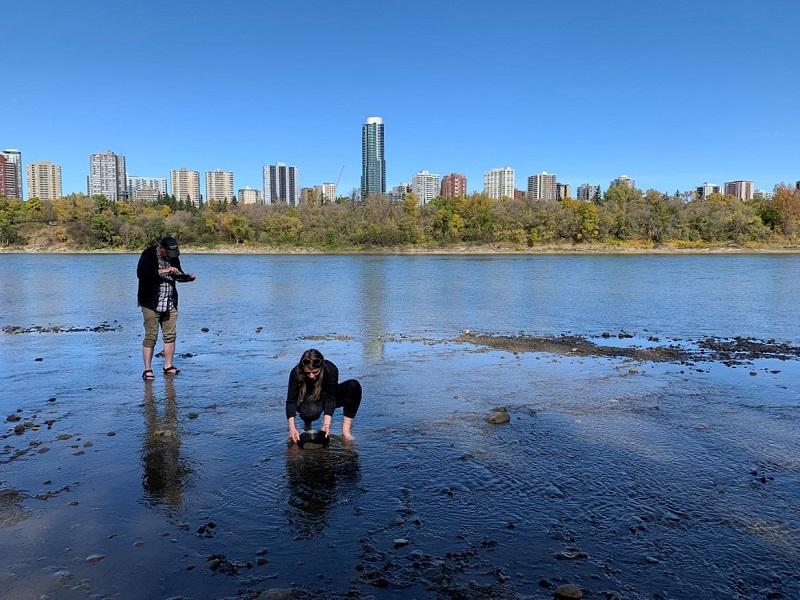 Two Royal Alberta Museum curators gold panning in the river valley with the Edmonton Skyline in the background