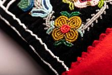 Detailed closeup of Indigenous beading. A gold flower with a red centre and green leaves is the design in the foreground.